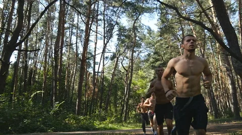 Group of young muscular athletes running at the forest path. Slow motion Stock Footage