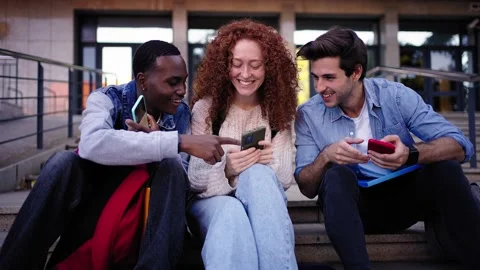 A group of young people are sitting on the steps of a building looking at their Stock Footage 268237109