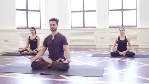 Group of young people doing yoga lotus pose in the class with windows Stock Footage 76182092