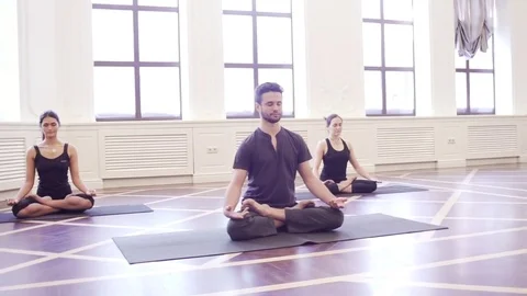 Group of young people doing yoga lotus pose in the class with windows Stock Footage 76182136