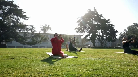 Group of young people practicing yoga on the seaside during the day. Green Grass Stock-Footage 110823405
