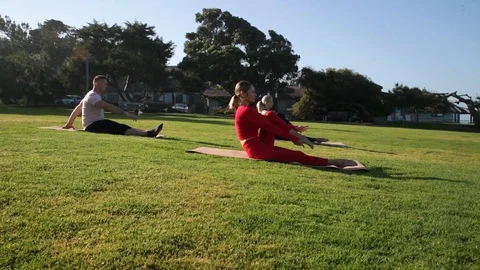 Group of young people practicing yoga on the seaside during the day. Green Grass Stock-Footage 110823527