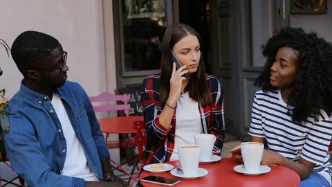 Group of young people sitting at table in cafe and talking.  One girl calling o Stock Footage 81836869