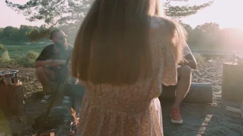 Group of young people talking while sitting around a fire on the river bank and 库存影片 237737915