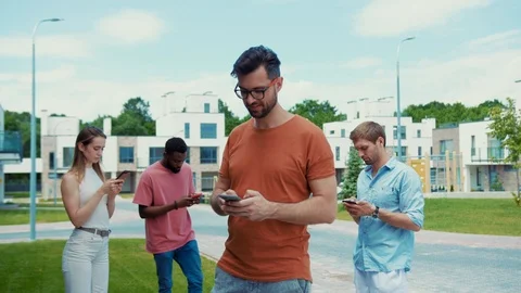 Group of young people using mobile phones while walking in the street. Focus on Видео 113796632