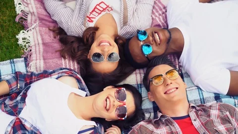 A group of young students are lying on a plaid blanket and laughing. Video stock 126282681
