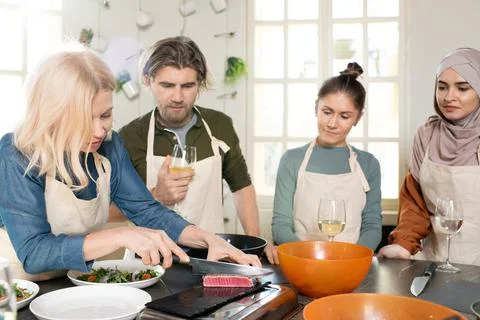 Group of young trainees in aprons looking at blond mature female cutting piece Stock Photos