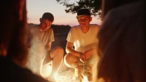 Groups of young people are talking and laughing while sitting around campfire 库存影片 224862362