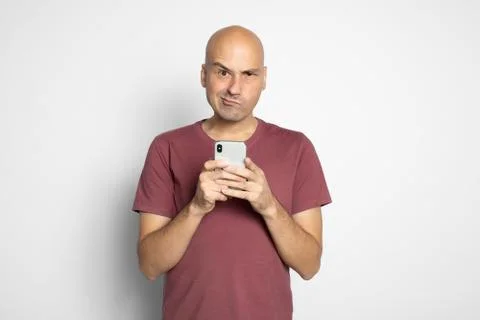 Grumpy bald man holding smartphone Foto stock