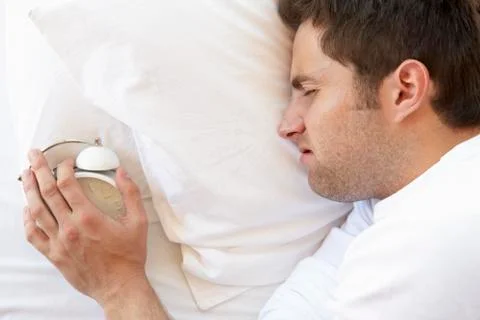 Grumpy Man In Bed Turning Off Alarm Clock Stock Photos