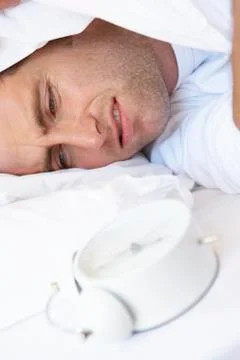 Grumpy Man In Bed Turning Off Alarm Clock Stock Photos