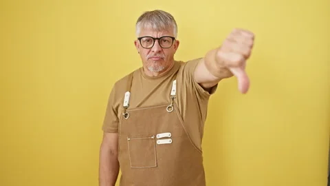 Grumpy middle-aged grey-haired man in apron and glasses showing thumbs down.. Stock Footage 275395375