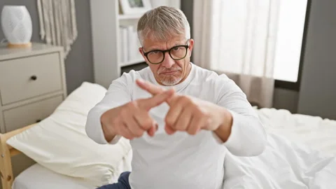 Grumpy middle-aged man, with grey hair, in pyjamas, waves a sign of rejecti.. Stock Footage 275396676