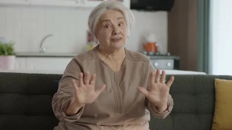 Grumpy old woman sitting on sofa at home giving thumbs up sign at camera. Stock Footage 190019306