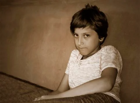 Grumpy young boy sitting on the couch leaning against the wall Stock Photos
