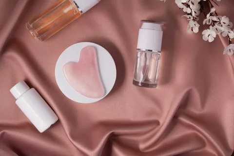 Gua sha massage scraper on a white podium and cometic products on shiny pink Stock Photos