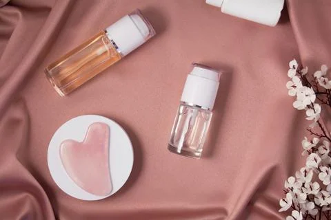 Gua sha massage scraper on a white podium and cometic products on shiny pink Stock Photos