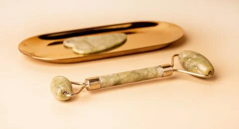 Gua Sha massage tools. Scraper and roller on golden stand and on beige Stock Photos