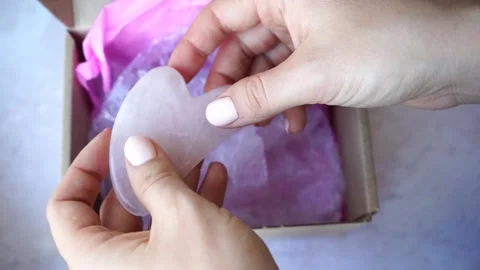 Gua Sha massager jade roller in female hands. Pink jade stone for face Stock Footage 150259399