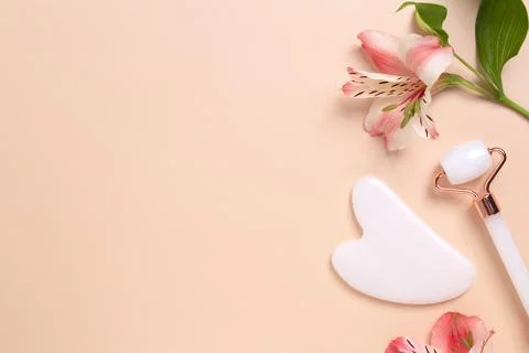 Gua sha stone, face roller for face massage on a beige background with flower Stock Photos