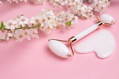 Gua sha stone, face roller for face massage on a pink background with bloomin Stock Photos
