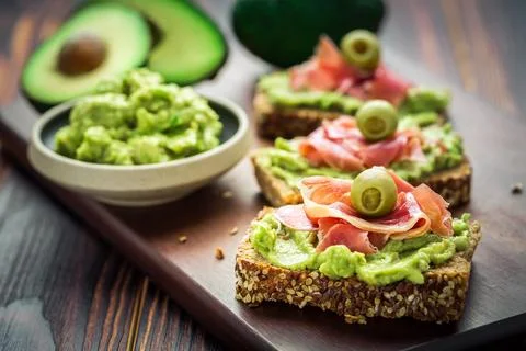Guacamole dip or spread with open sandwiches and ham on wooden kitchen table Foto stock