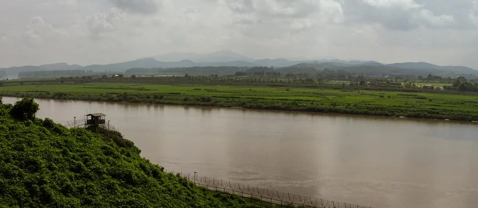 Guard Post Overlooking Tranquil River And Green Fields With Mountain Range .. Stock Photos