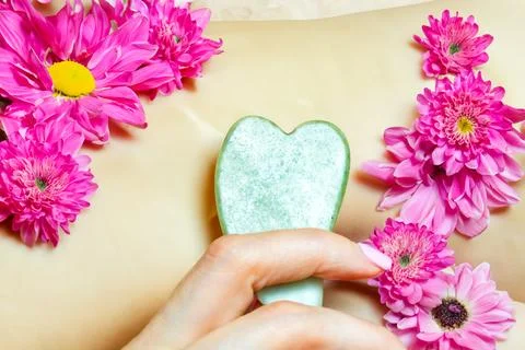Guasha face massage with jade green stone In a woman's hand.Close-up with flower Stock Photos