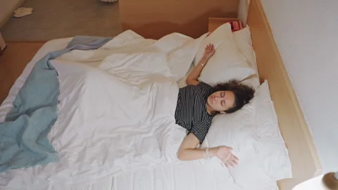 Guest gently rises from bed in peaceful hotel chamber. Individual enjoying 库存影片 334629265