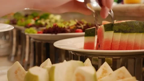 A guest picks pieces of watermelon with serving tongs from a fruit tray and Stock Footage 332300860