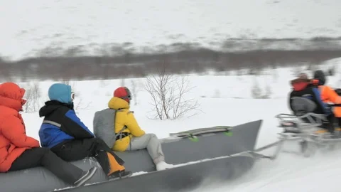 Guide drives snowmobile pulling long grey snow banana boat Stock Footage 109116014