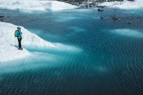 Guide standing on the edge of a deep blue lake on top of a glacier in Alaska. Stock Photos
