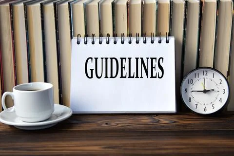 GUIDELINES - word on white notebook on background of books, clock and cup o.. Stock Photos