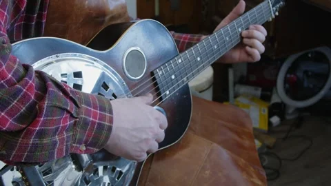 Guitar tech in leather apron plays National Steel guitar in work shop Stock Footage 331986211