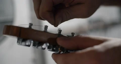 Guitar tech takes off the old strings from the guitar tuners, changing the Stock Footage 163966494