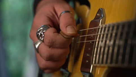 Guitarist's hand with rings picking the strings of a yellow electric guitar Stock Footage 336622648
