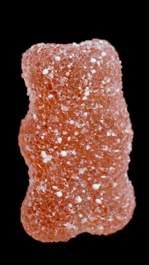 A gummy candy in the shape of a bear, dusted with sugar. It rotates on a black b 스톡 동영상 249607461