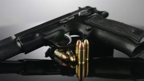 Gun Control. 9mm handgun with bullets rotating on a reflective surface Stock Footage 202914714