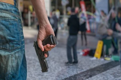 Gun control concept. Armed man - attacker holds pistol in hand in public plac Stock Photos