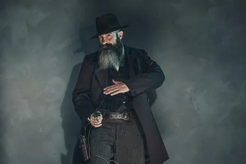 Gun shooting vintage crook with long beard in 1900 style clothing against gre Foto stock