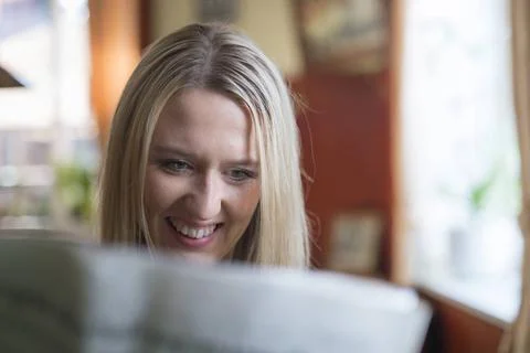 Gute Nachrichten Eine junge Frau sitzt am Fenster und liest amüsiert die Z.. Stock Photos