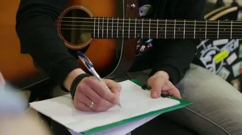 Guy with an acoustic guitar writes chords on a sheet Stock Footage 62505805