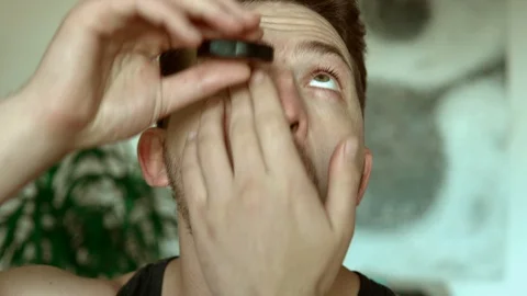 Guy administers eye drops to alleviate irritated dry eye. Water drop makes Video stock 91552589