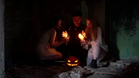 A guy and two girls in the form of a vampires on Halloween warm hands on candles Stock Footage 97038540