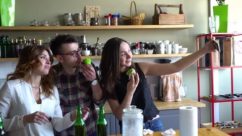 A guy and two girls make selfies in the kitchen with cupcakes and beer Stock Footage 75233365