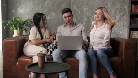 Guy and two girls sit on sofa with laptop making video call greeting friend. Stock Footage 198877055