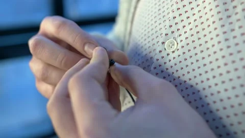 The guy attaches a small black microphone to his light-colored shirt. Close-up. Video stock 136154487