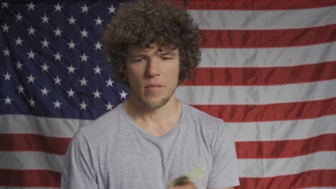 Guy in the background of the American flag holds dollars in his hands. He's Video stock 139464939