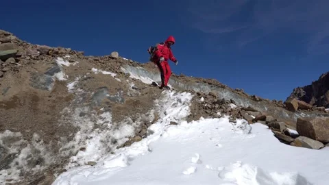 A guy with a backpack goes down glacier with rocks Video stock 234514961