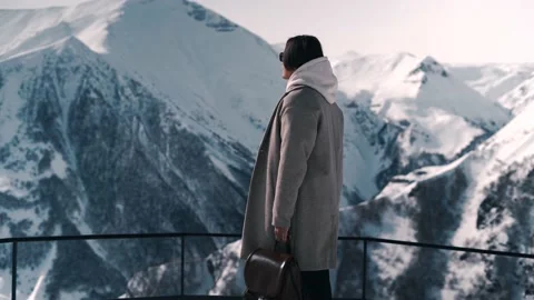 A guy with a backpack in his hands looks at the mountains Stock Footage 169814640